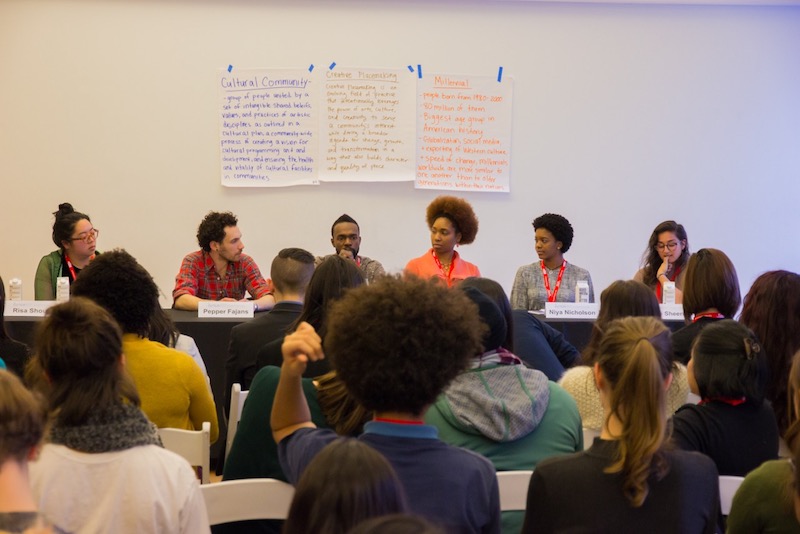 A group of people sit in the audience in front of the Creative Placemaking: The Role of Millennial Artists Panel